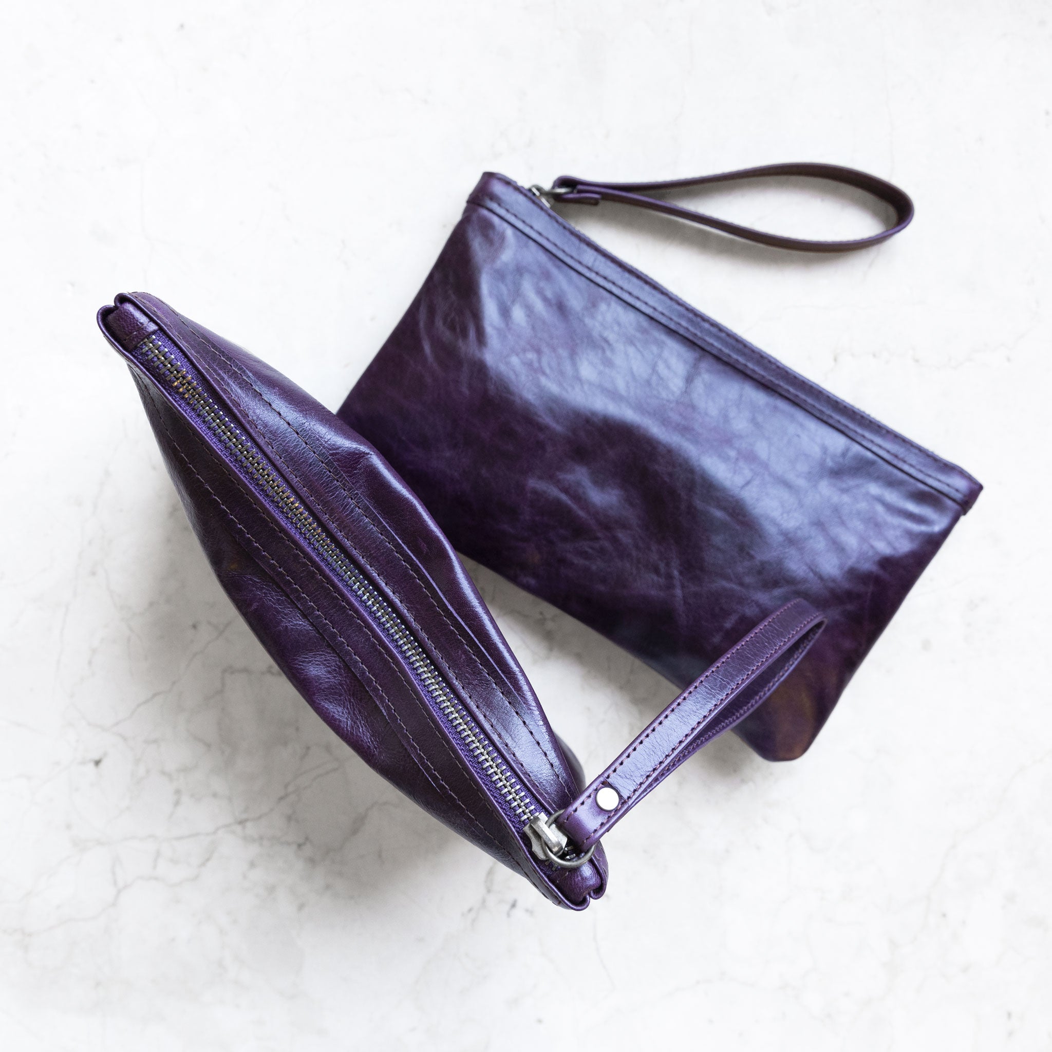 alex wristlet clutches, size medium shown, in aubergine, one laying flat and one standing to show top zipper