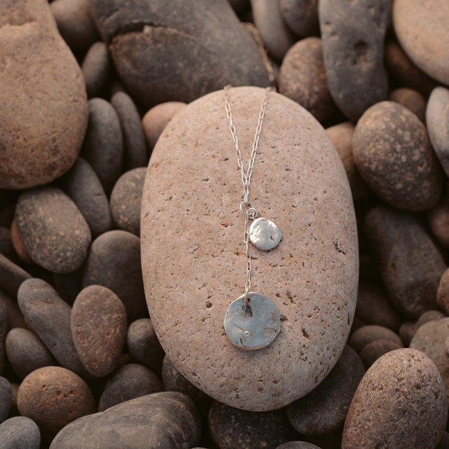 general | andromeda silver lariat necklace atop a beach stone