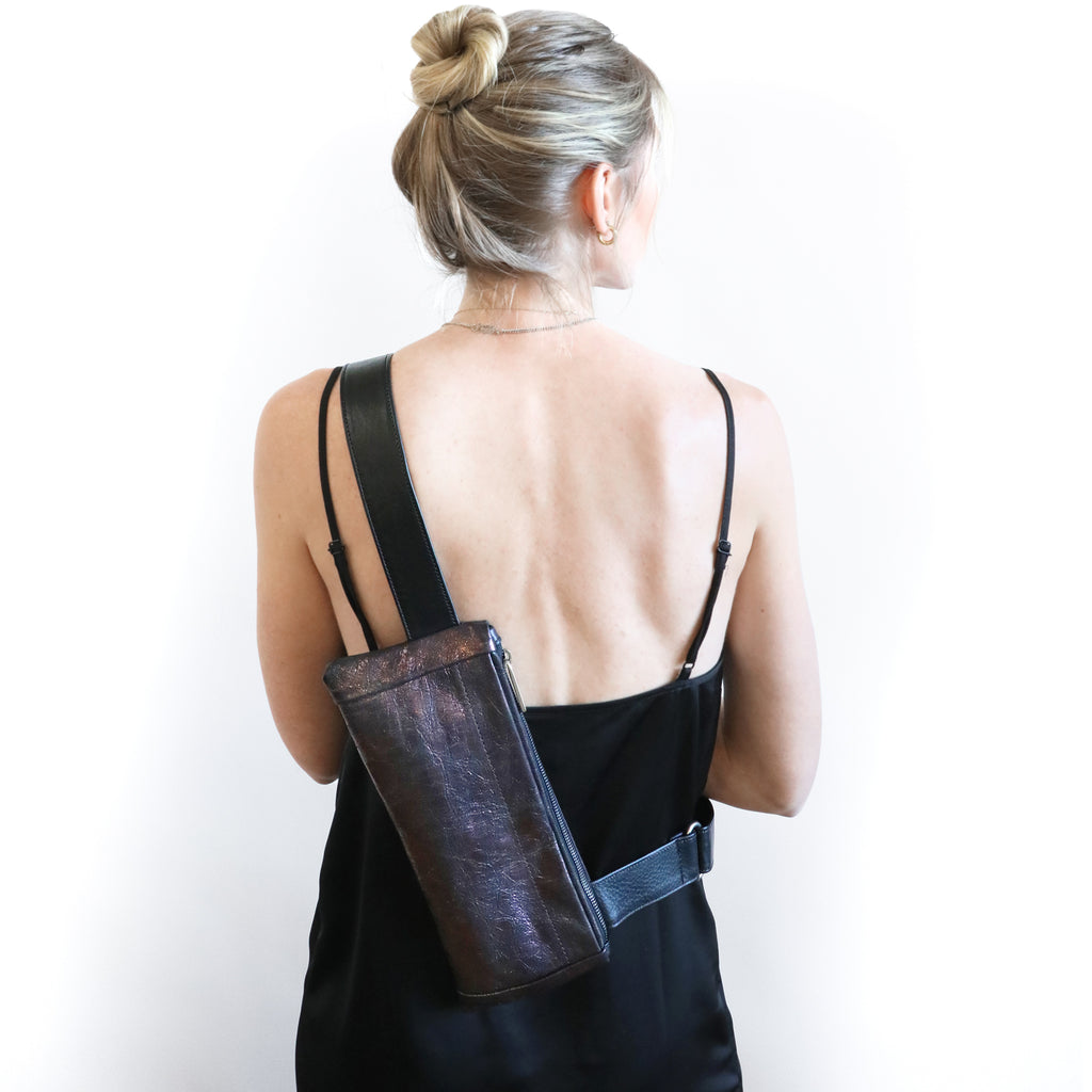 Back view of model wearing district sling in mica amethyst and black crossbody. 