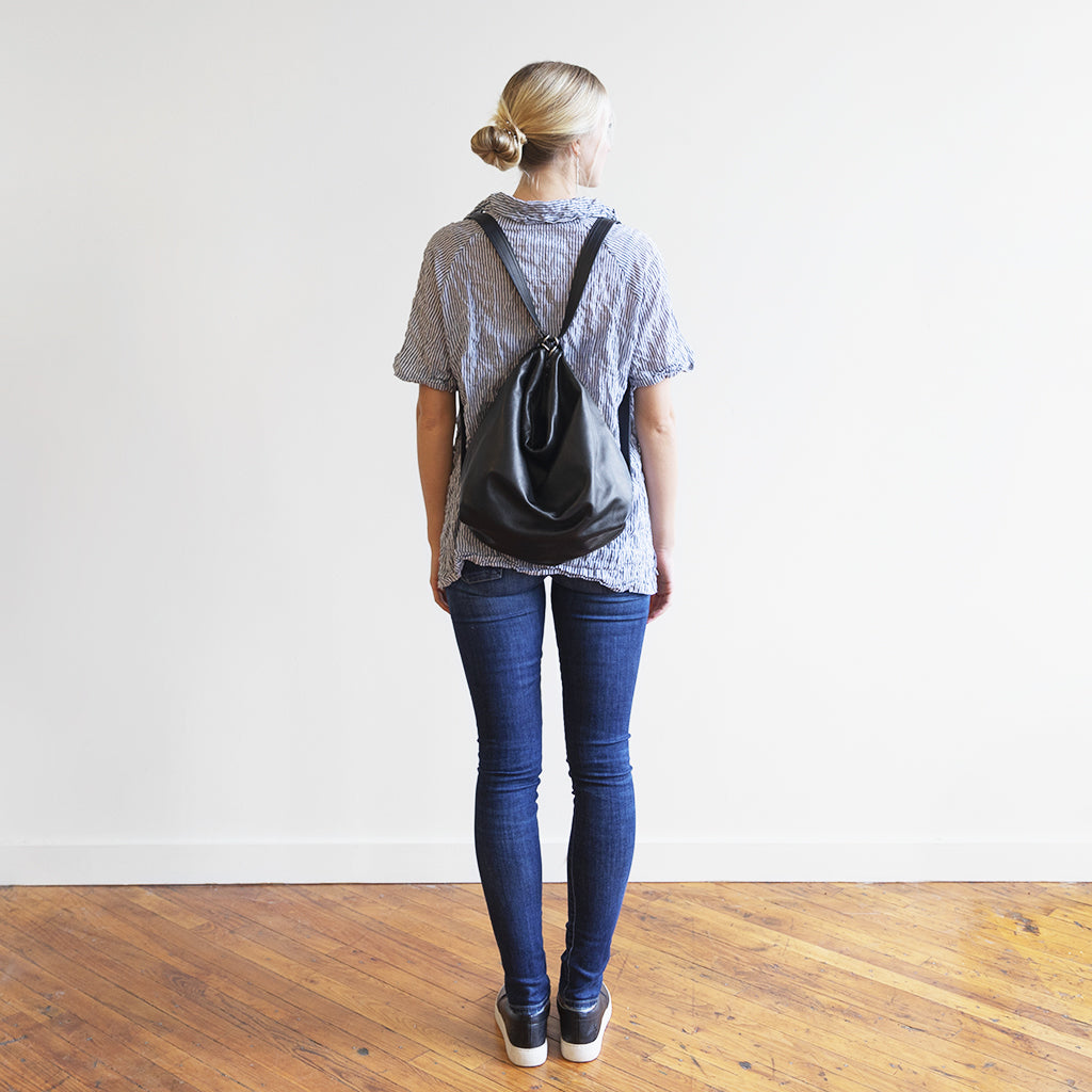 Back view of a model with a hobo pack original, size extra large, showing strap adjusted for backpack carry. 