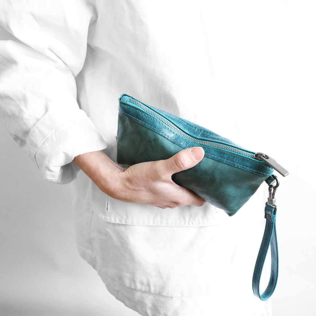 Close-up of model holding a zip pouch medium in rodeo teal and tourmaline. 